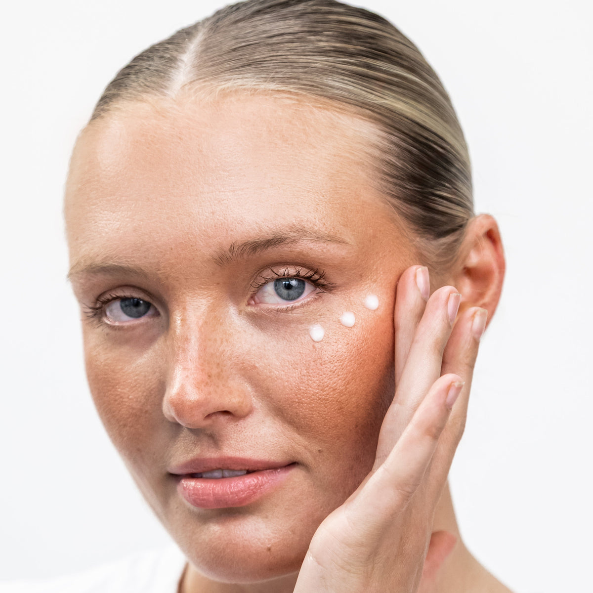 Model with dots of Plush Glow Eye Cream applied under her eye